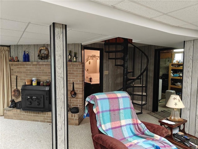 finished basement featuring carpet floors, a wood stove, wood walls, and a paneled ceiling