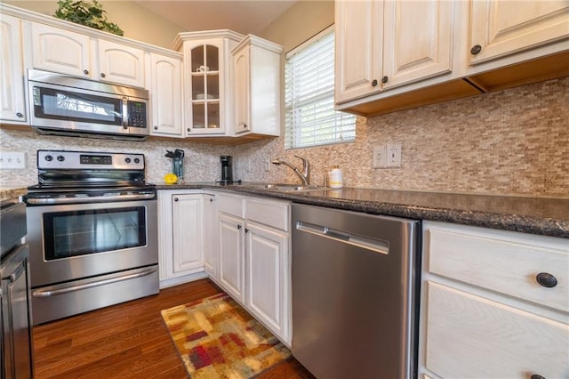 kitchen with backsplash, appliances with stainless steel finishes, wood finished floors, a sink, and glass insert cabinets
