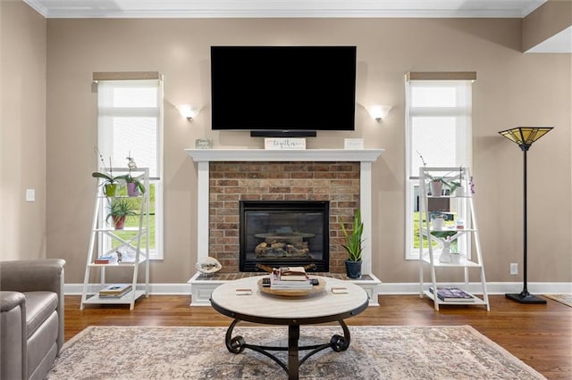 living room with crown molding, baseboards, a brick fireplace, and wood finished floors