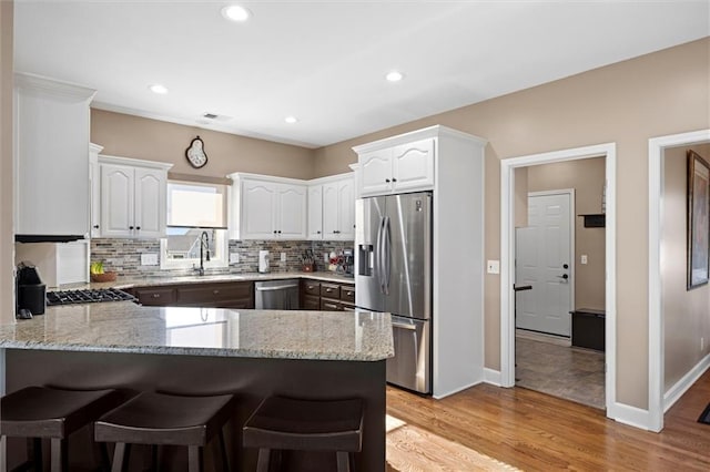 kitchen featuring a peninsula, backsplash, light stone countertops, and stainless steel appliances