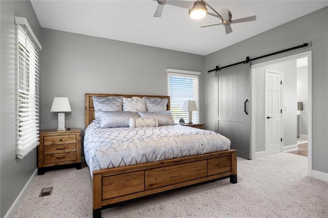 carpeted bedroom with baseboards, a barn door, ceiling fan, and visible vents