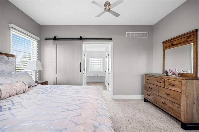 bedroom featuring visible vents, light speckled floor, baseboards, a barn door, and connected bathroom
