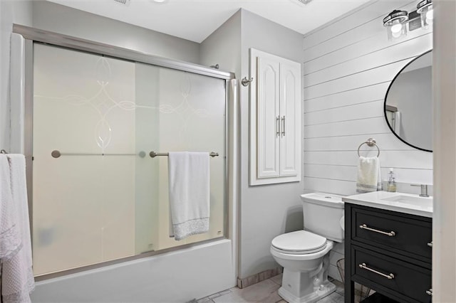 full bath with bath / shower combo with glass door, tile patterned floors, vanity, toilet, and wooden walls