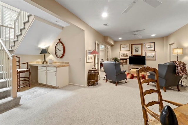 living room featuring visible vents, light carpet, a ceiling fan, and stairway