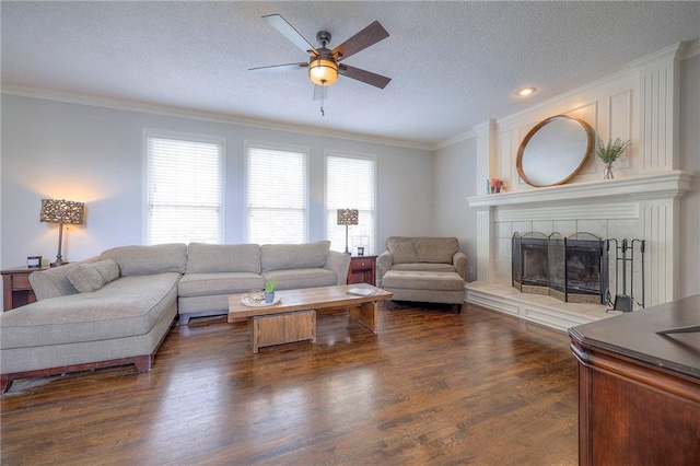 living area featuring a ceiling fan, a textured ceiling, crown molding, a fireplace, and dark wood-type flooring