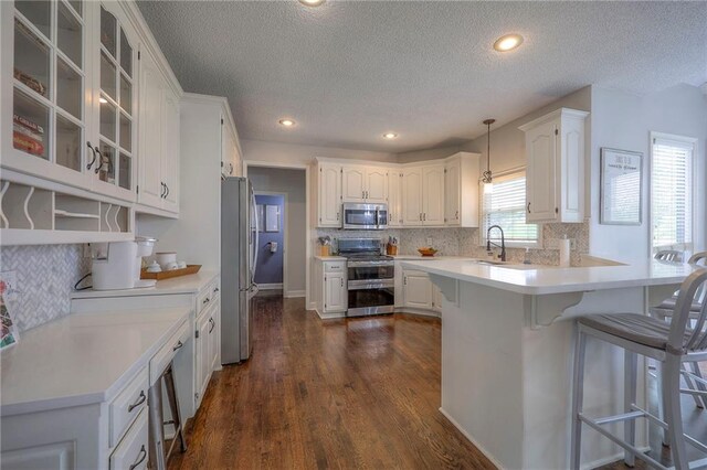 kitchen featuring a kitchen bar, a textured ceiling, a sink, stainless steel appliances, and white cabinetry