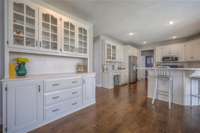 kitchen with glass insert cabinets, a kitchen bar, a textured ceiling, white cabinetry, and appliances with stainless steel finishes