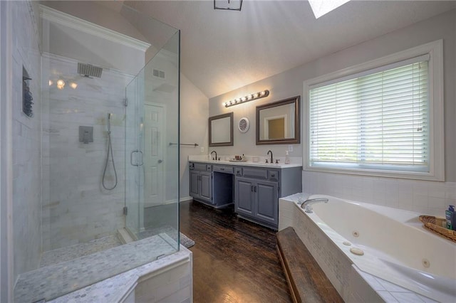 bathroom featuring double vanity, lofted ceiling, a jetted tub, a sink, and a stall shower