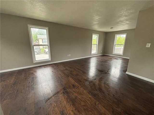 empty room with dark wood-style flooring, a textured ceiling, and baseboards
