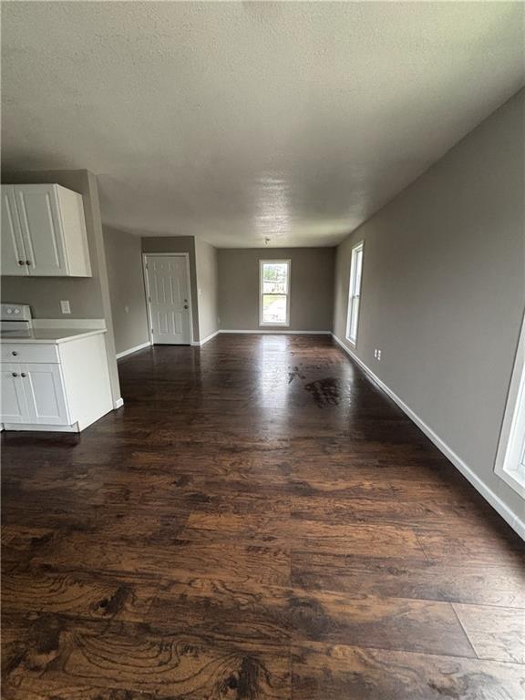 unfurnished living room featuring baseboards, a textured ceiling, and dark wood-type flooring