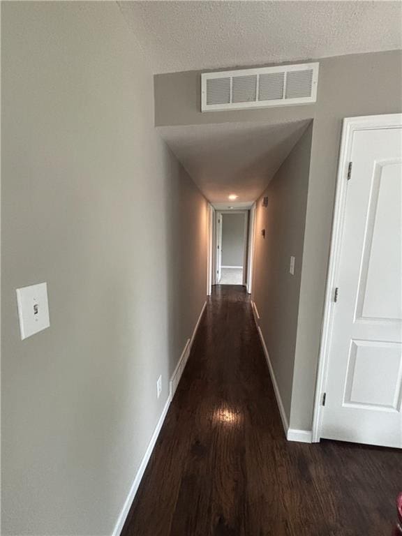 hall featuring dark wood-style flooring, visible vents, a textured ceiling, and baseboards