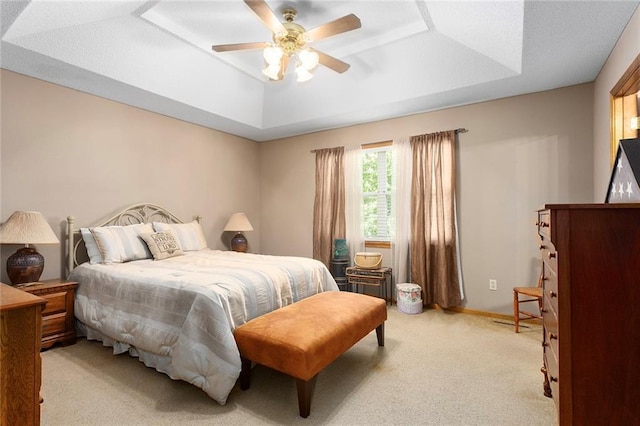 bedroom featuring a tray ceiling, light colored carpet, and a ceiling fan