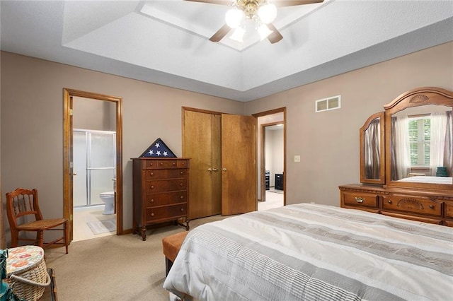 bedroom with light colored carpet, ensuite bathroom, a closet, a ceiling fan, and a tray ceiling