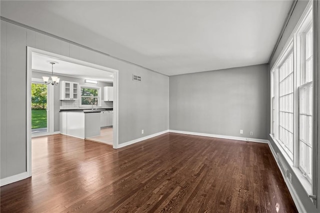 unfurnished living room with a chandelier, dark wood-style flooring, and baseboards