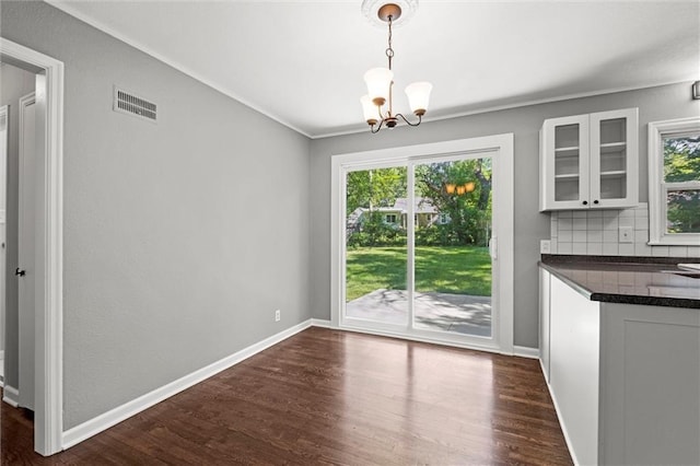 unfurnished dining area with a chandelier, healthy amount of natural light, dark wood-type flooring, and ornamental molding