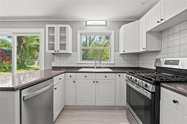 kitchen with stainless steel appliances, a sink, dark countertops, white cabinets, and a peninsula