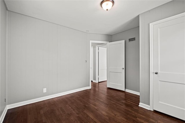 unfurnished bedroom with dark wood finished floors, baseboards, and a decorative wall