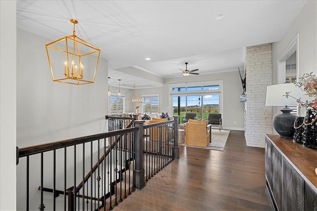 corridor with an upstairs landing, dark wood finished floors, baseboards, a chandelier, and ornamental molding