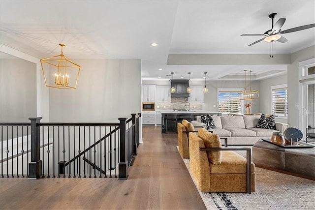 living room featuring recessed lighting, crown molding, ceiling fan with notable chandelier, and wood finished floors