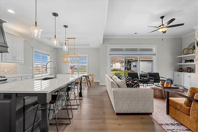 living room with a ceiling fan, baseboards, light wood finished floors, ornamental molding, and recessed lighting
