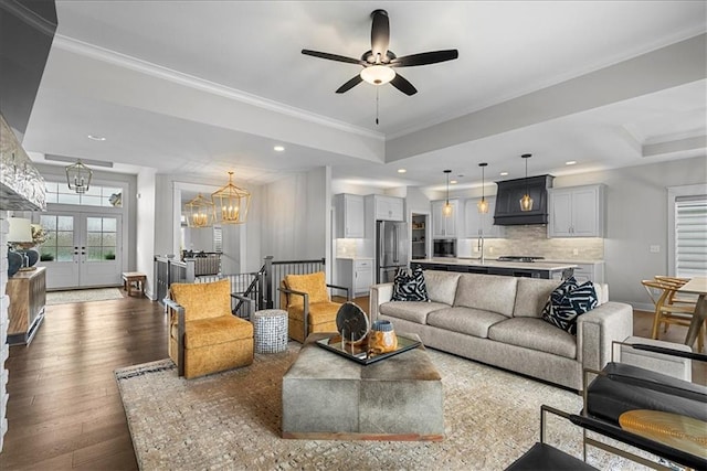 living room featuring french doors, dark wood-style flooring, crown molding, ceiling fan with notable chandelier, and a tray ceiling