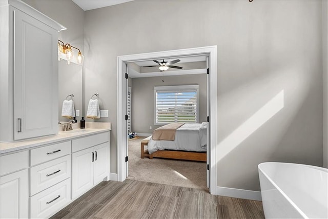 bathroom featuring vanity, wood finished floors, baseboards, a freestanding bath, and a ceiling fan
