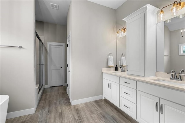 full bath featuring a sink, a shower stall, double vanity, and wood finished floors