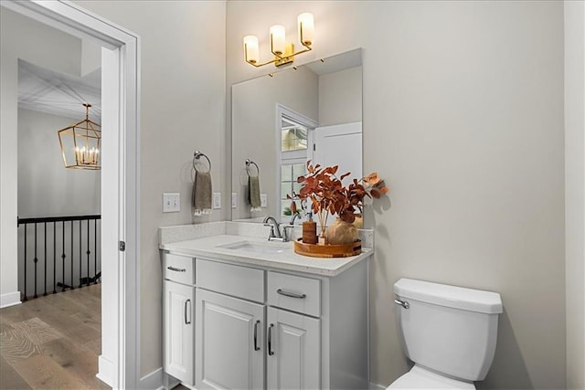 half bathroom featuring an inviting chandelier, wood finished floors, toilet, and vanity