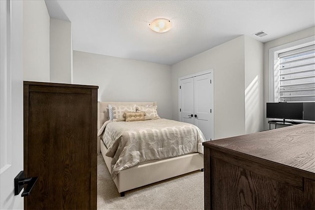 bedroom featuring light colored carpet, visible vents, and a closet