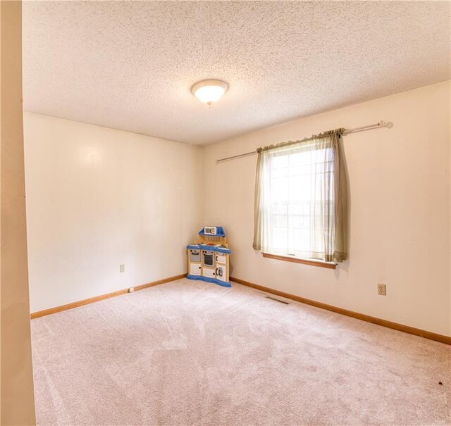 spare room featuring carpet floors, baseboards, a textured ceiling, and visible vents