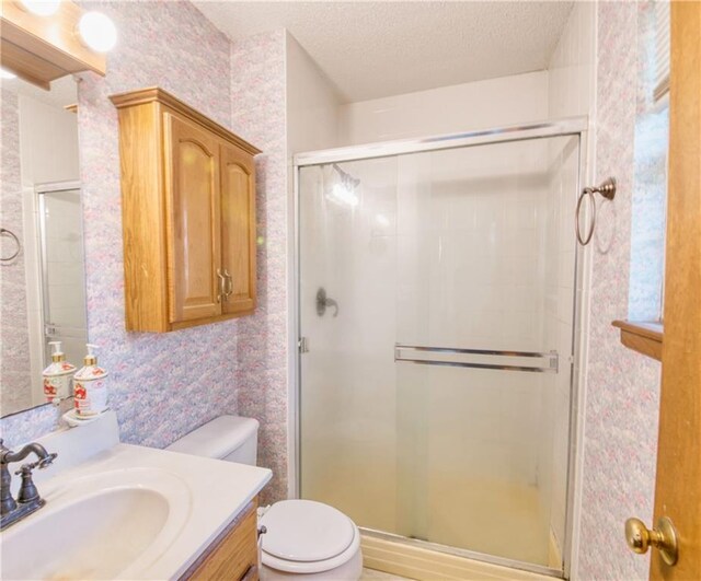 bathroom with vanity, toilet, wallpapered walls, a textured ceiling, and a stall shower