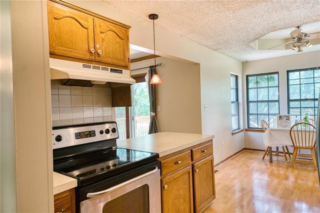 2109 NW Hidden Pointe Ct, Blue Springs, MO 64015 - kitchen with stainless steel electric range oven, under cabinet range hood, a textured ceiling, brown cabinets, and healthy amount of natural light