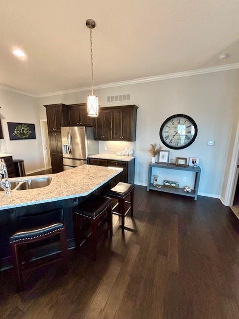 kitchen with dark brown cabinets, a sink, stainless steel fridge with ice dispenser, a kitchen bar, and dark wood-style floors