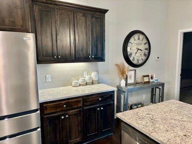 kitchen with freestanding refrigerator, light stone countertops, dark brown cabinetry, and tasteful backsplash
