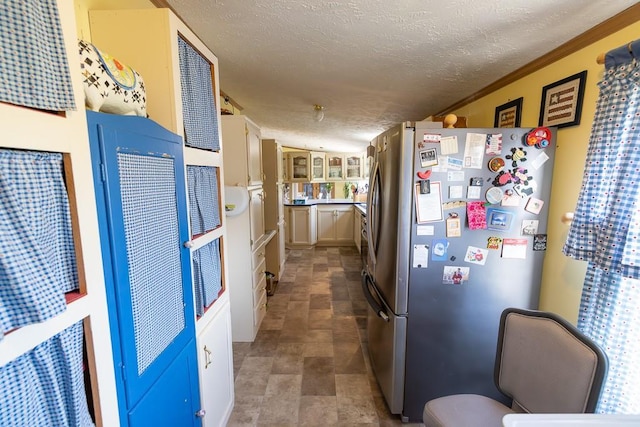 kitchen with glass insert cabinets, crown molding, stone finish floor, a textured ceiling, and freestanding refrigerator