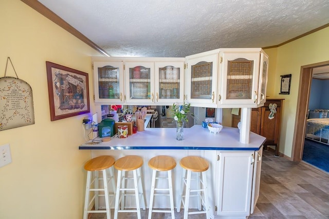 kitchen with a breakfast bar area, a peninsula, crown molding, and glass insert cabinets