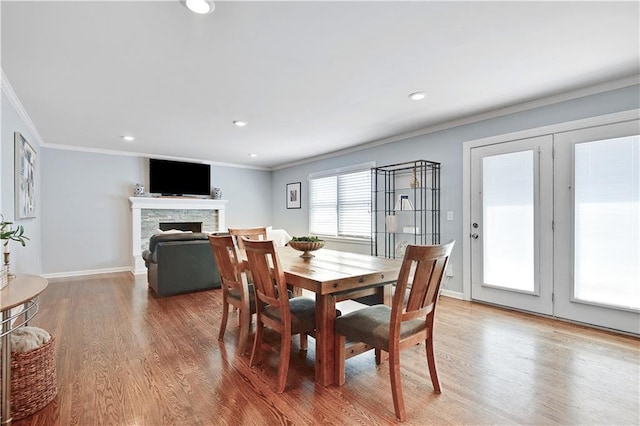 dining room featuring a fireplace, recessed lighting, baseboards, wood finished floors, and ornamental molding