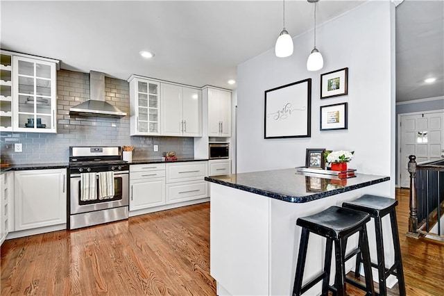 kitchen featuring decorative backsplash, dark countertops, a kitchen bar, wall chimney exhaust hood, and stainless steel appliances