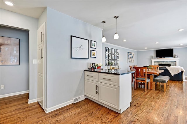 kitchen featuring baseboards, a peninsula, wood finished floors, and dark countertops