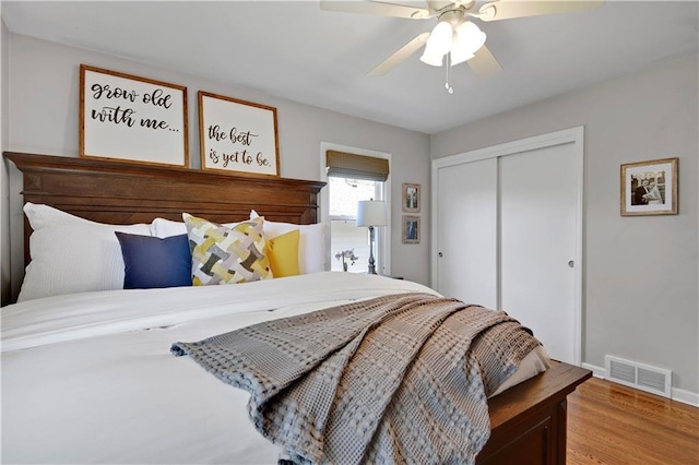 bedroom featuring visible vents, a closet, wood finished floors, baseboards, and a ceiling fan
