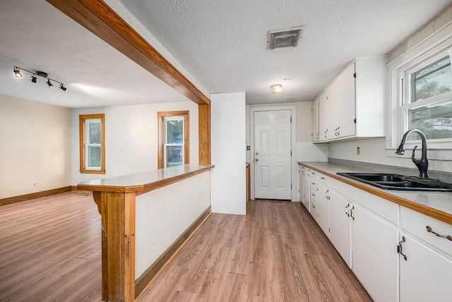 kitchen featuring a sink, light wood-style floors, light countertops, white cabinetry, and baseboards