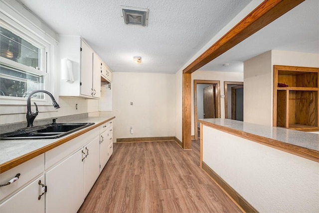 kitchen with a sink, light countertops, light wood-type flooring, and white cabinetry