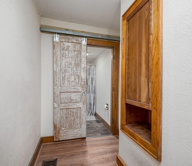 corridor featuring baseboards, visible vents, a barn door, and wood finished floors