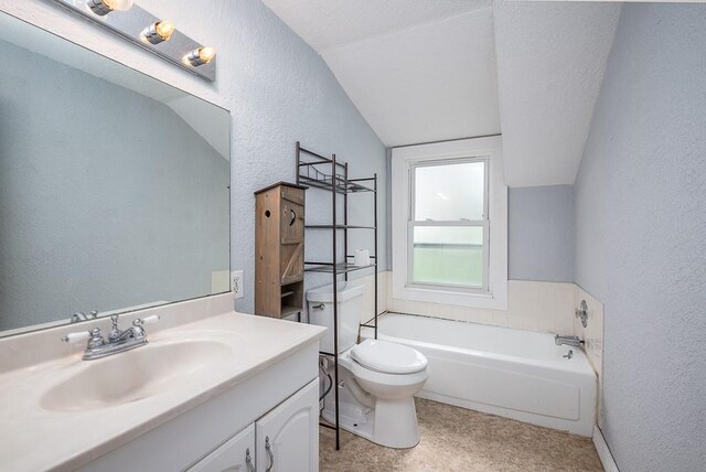 bathroom with a garden tub, vanity, toilet, lofted ceiling, and a textured wall