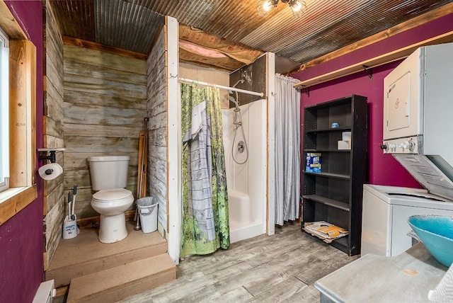 bathroom featuring wooden walls, toilet, a shower with shower curtain, stacked washer / dryer, and wood finished floors