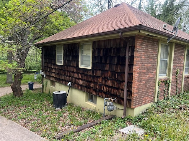 view of property exterior featuring brick siding, central AC unit, and roof with shingles