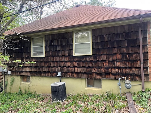 view of property exterior featuring a shingled roof and central AC