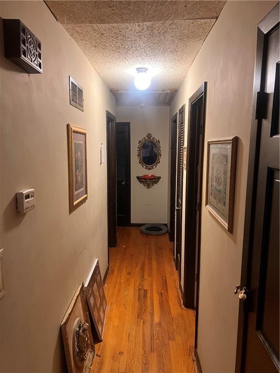 hall with visible vents, a textured ceiling, and light wood-style flooring