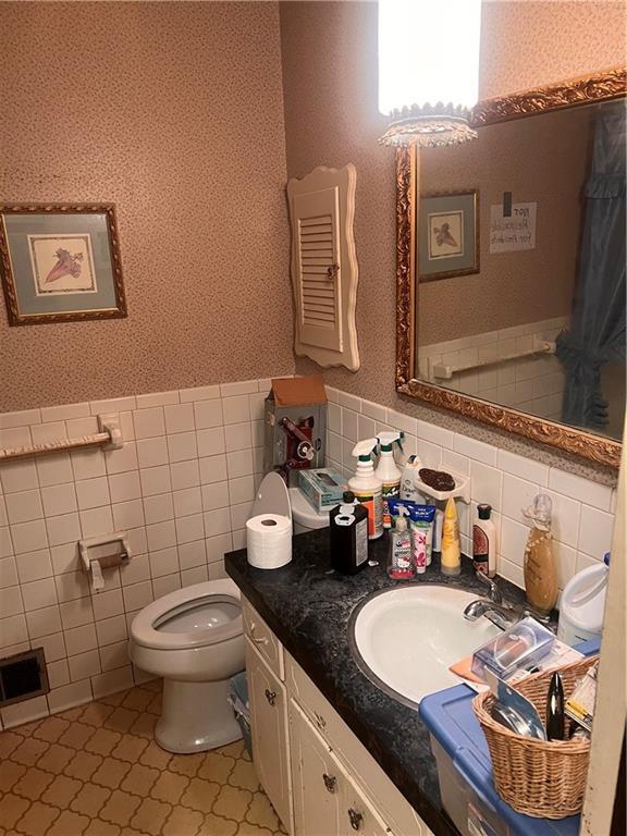 bathroom featuring vanity, visible vents, toilet, tile walls, and a wainscoted wall