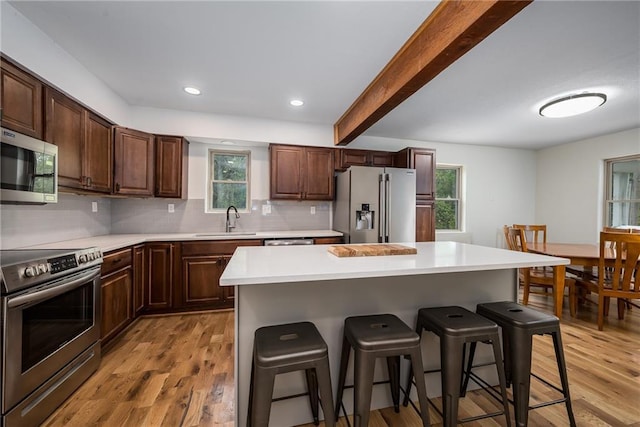 kitchen featuring appliances with stainless steel finishes, a sink, a breakfast bar area, a healthy amount of sunlight, and light wood-type flooring